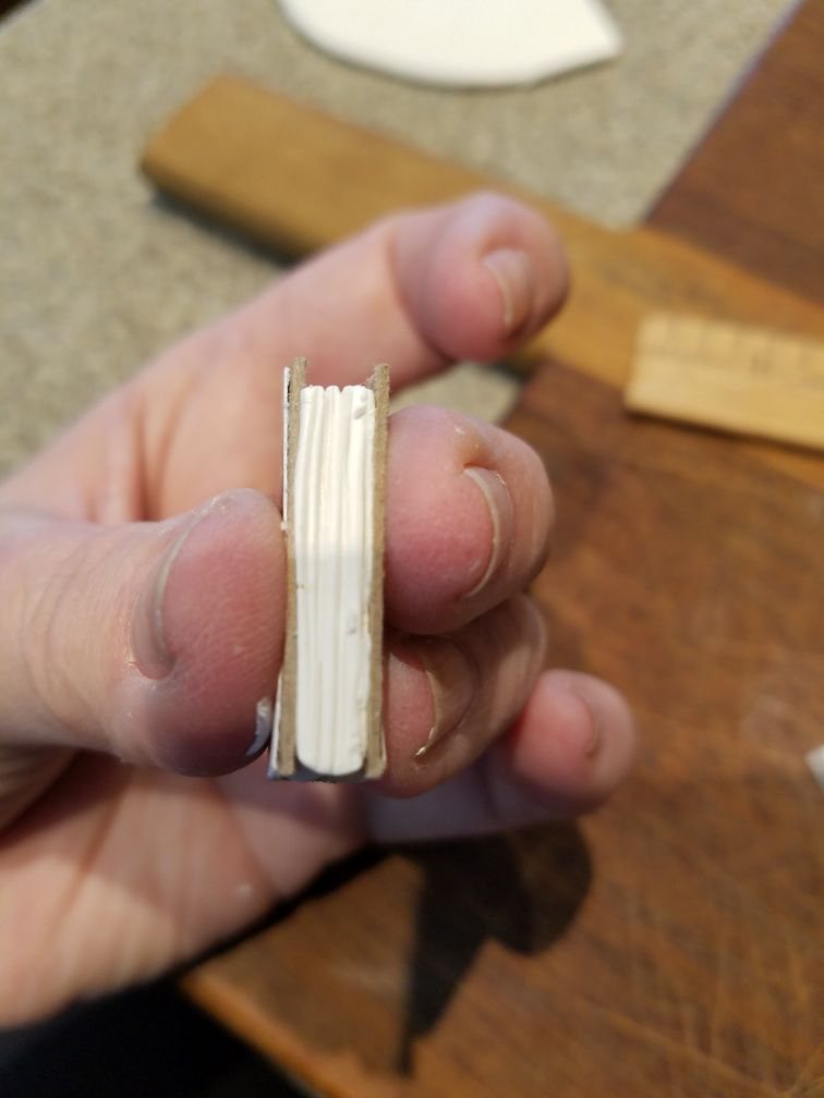 A hand holding a mini book with its cardboard cover glued around the white clay pages